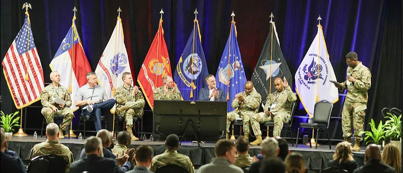 Uniformed and civilian panelists on stage in front of the United States flag and service flags at the chapter's Innovation Summit