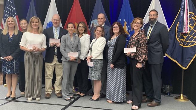 Grant and scholarship recipients standing on stage with chapter leadership in front of the United States flag
